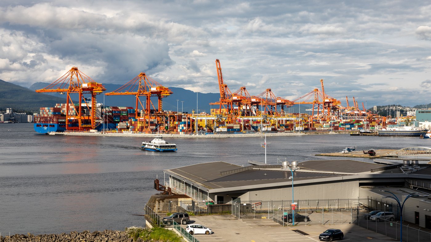 Gantry cranes and stacked shipping containers at the Centerm container terminal in Vancouver, with the North Shore mountains behind